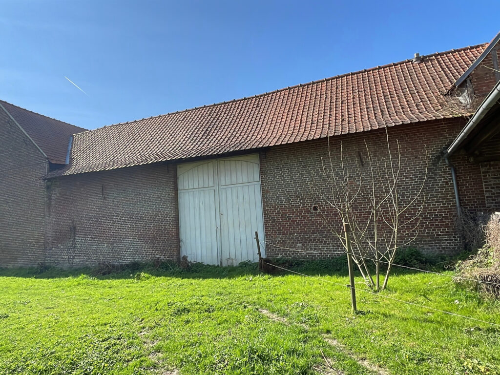 Façade extérieure d’une grange en brique avec grande ouverture et potentiel de stockage