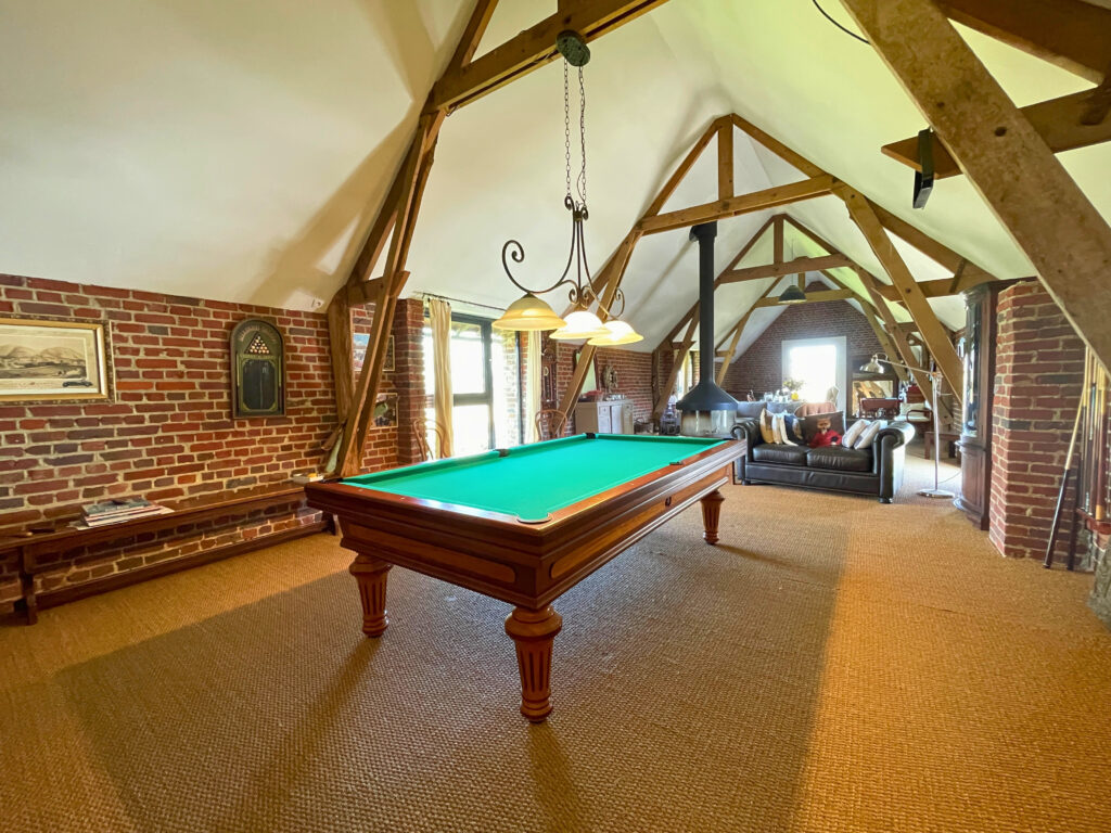 Vue d’ensemble du grand salon, espace de 80 m² à l’étage avec poutres apparentes, cheminée centrale et belle hauteur sous plafond