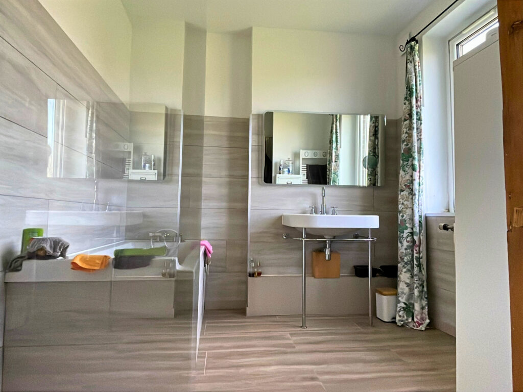 Salle de bains équipée d’une baignoire, d’une douche séparée, d’une vasque et de rangements, dans un espace lumineux et fonctionnel