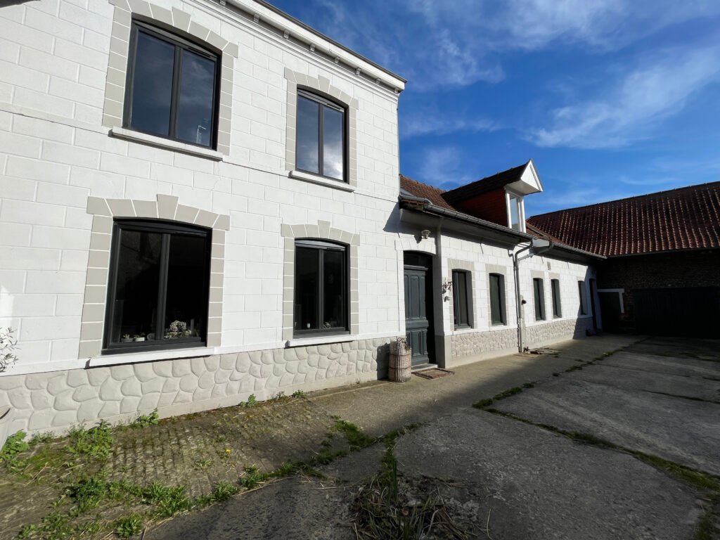 Façade blanche de l’habitation principale, typique des fermes au carré, ouvrant sur la cour intérieure pavée et l’entrée centrale