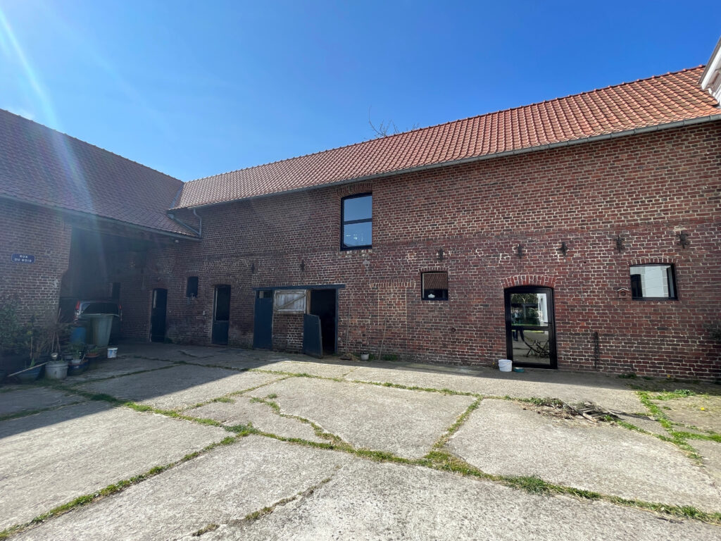 Perspective depuis la cour intérieure vers les salons de la maison principale, façade briques rouges et ouvertures vitrées alu visibles
