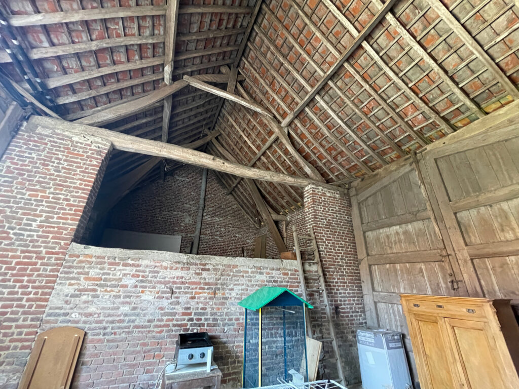 Vue en hauteur de la grange attenante, montrant la charpente, la couverture en tuiles et le film noir de protection visible sous la toiture surface au sol 93 m2