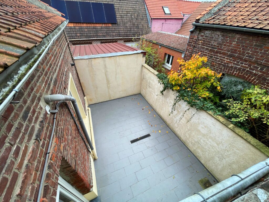 Vue depuis l’étage sur la cour de 22 m² orientée Est, maison en briques à Raimbeaucourt avec murs clairs et végétation