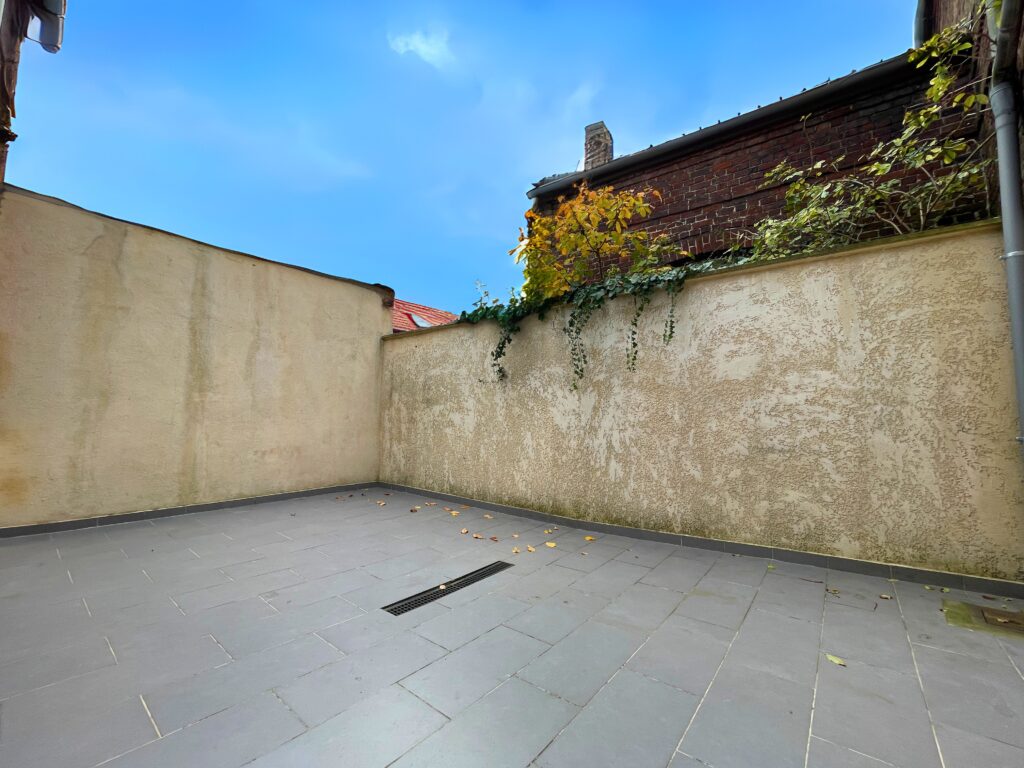 Cour extérieure carrelée, murs enduits et ciel dégagé, espace calme et lumineux de la maison à vendre à Raimbeaucourt