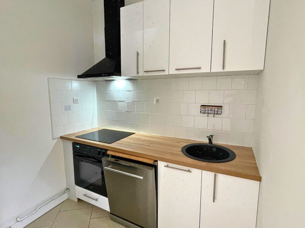 Cuisine fonctionnelle avec plaque induction, four encastré, hotte noire et lave-vaisselle, maison rénovée à Raimbeaucourt