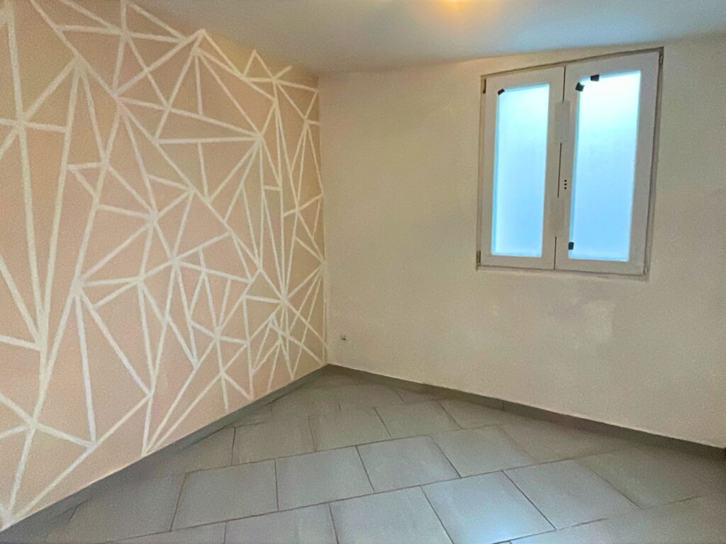 Chambre ou espace bureau du studio indépendant, carrelage clair et mur géométrique décoratif, maison à vendre à Raimbeaucourt