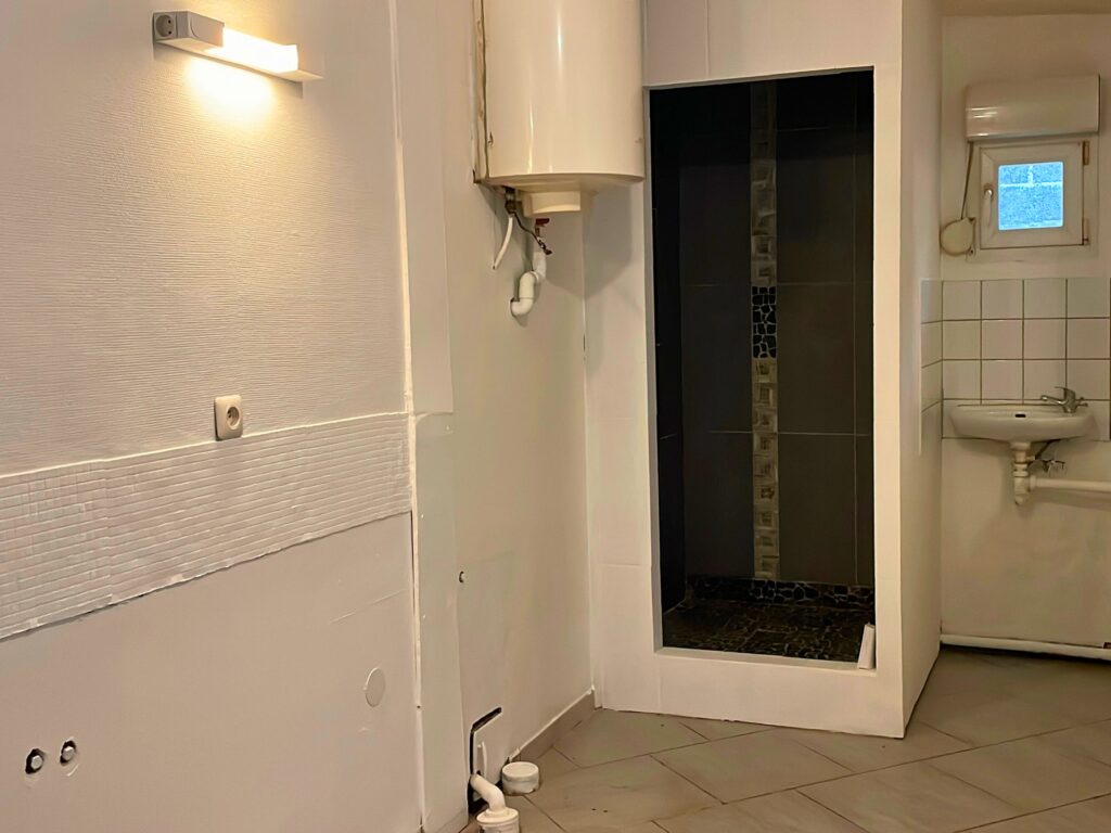 Espace d’eau du studio avec douche, lavabo et ballon d’eau chaude, idéal pour réhabilitation ou projet locatif à Raimbeaucourt