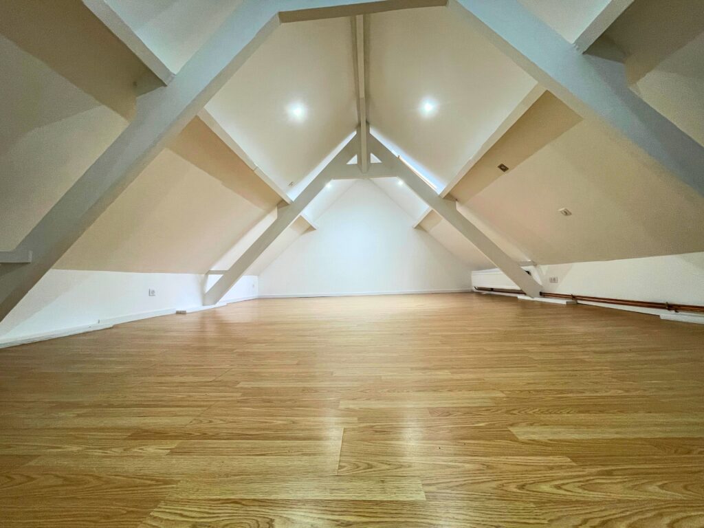 Chambre mansardée spacieuse sous combles, 37 m² au sol, poutres apparentes blanches et parquet clair, maison à vendre à Raimbeaucourt