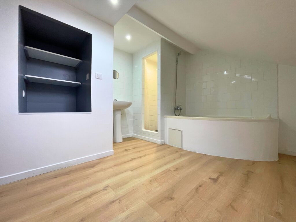 Salle de bain rénovée sous combles avec baignoire d’angle, vasque et niche murale, parquet stratifié clair, maison à vendre à Raimbeaucourt