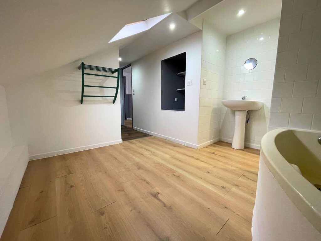 Salle de bain spacieuse sous combles avec baignoire, lavabo et rangements muraux, parquet clair et mur carrelé blanc, maison rénovée à Raimbeaucourt